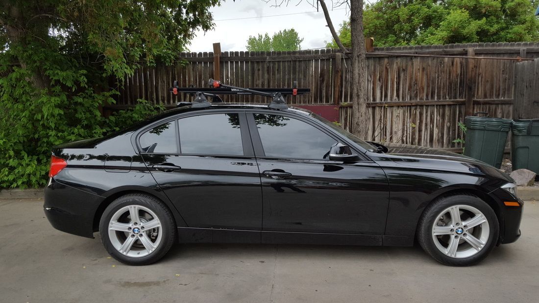 A black car with a roof rack is parked in front of a wooden fence.