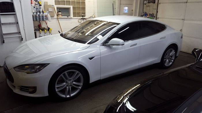 A white tesla model s is parked in a garage next to a black car.