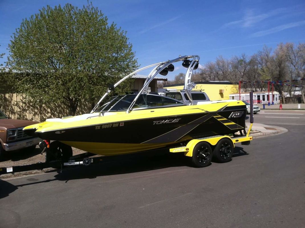 A yellow and black boat on a trailer is parked on the side of the road.