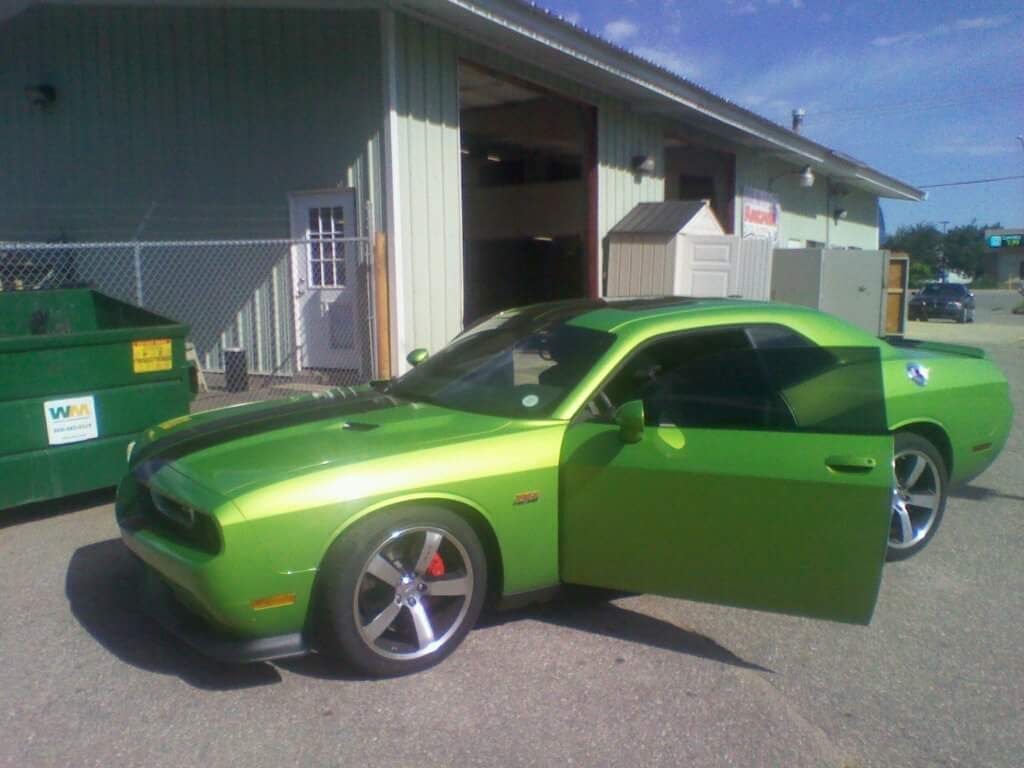 A green dodge challenger is parked in front of a building