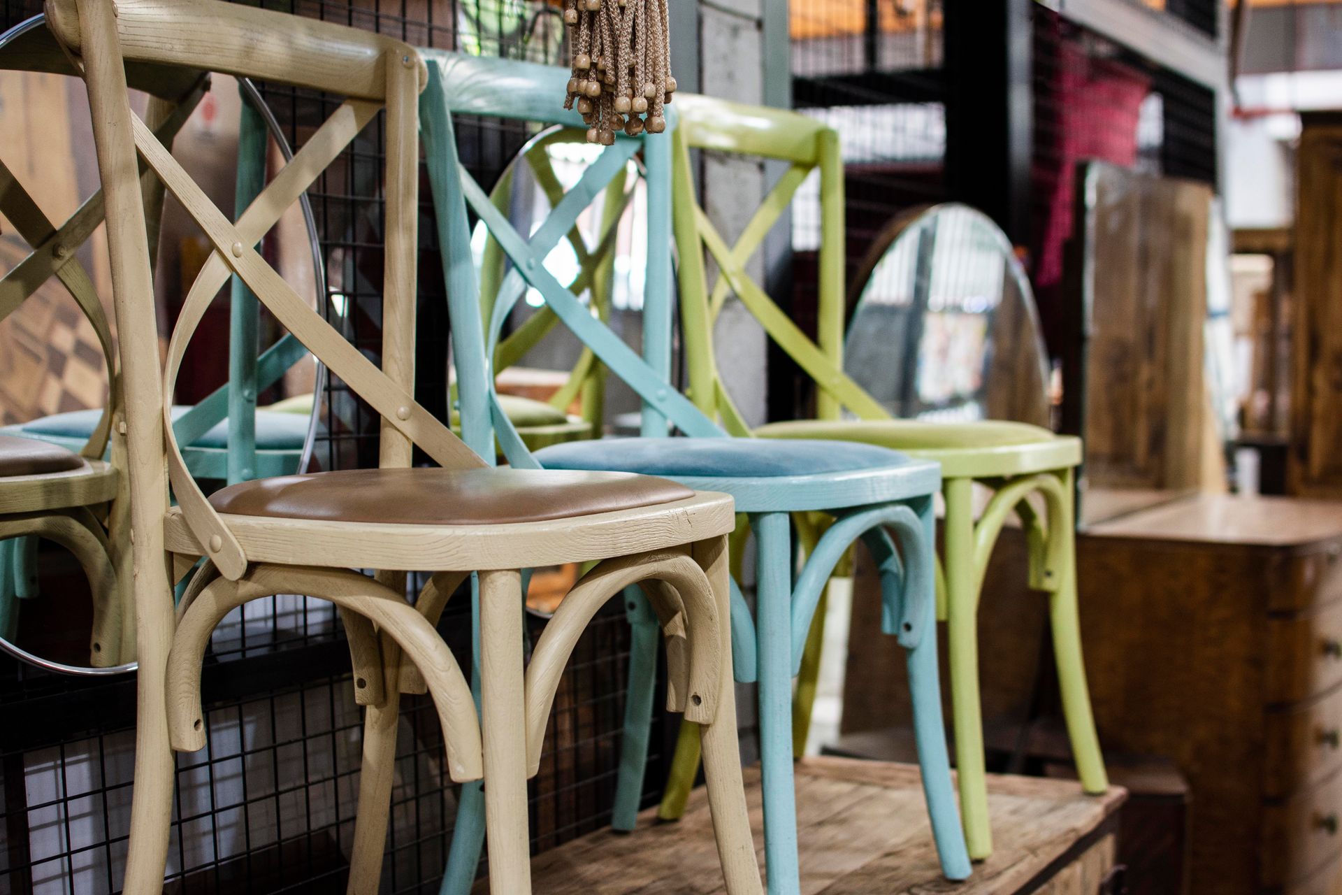 Four colorful wooden cross-back chairs in pastel shades: beige, blue, and green.