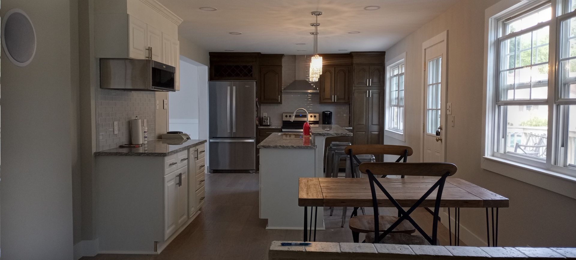 Bright kitchen and dining area with stainless steel appliances, dark cabinets, and large windows.