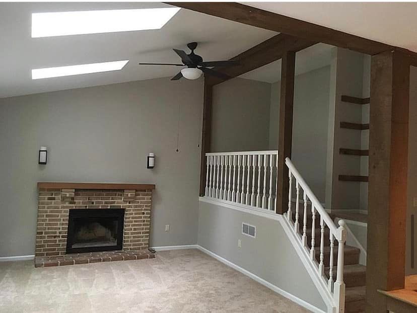 Empty living room with brick fireplace, skylights, ceiling fan, and white staircase railing