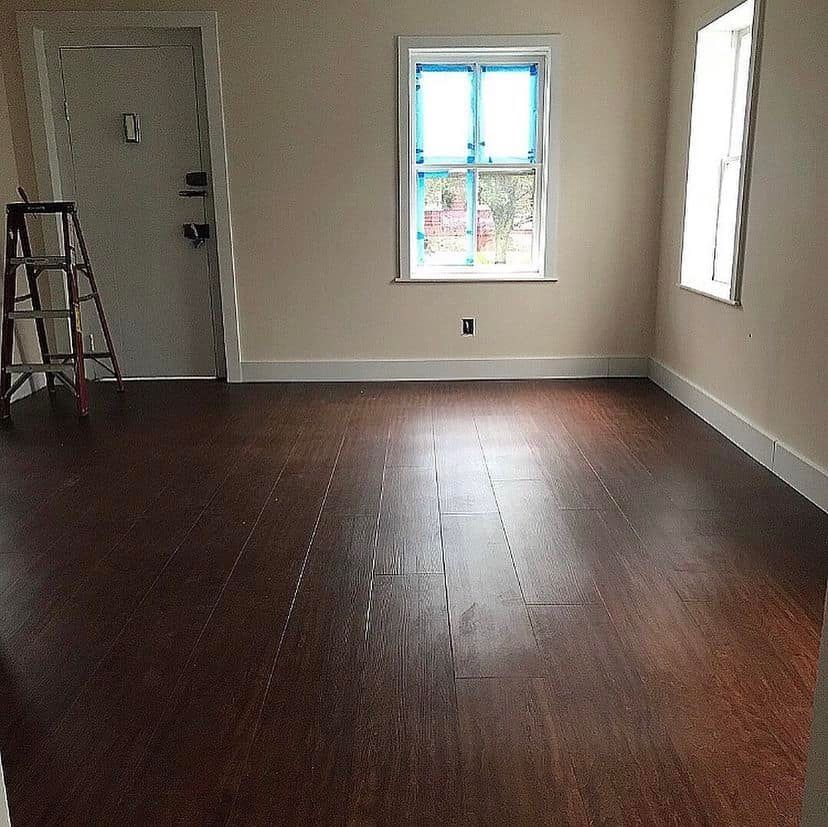 Empty room with dark wood floors, white walls, a window, and a ladder near the door