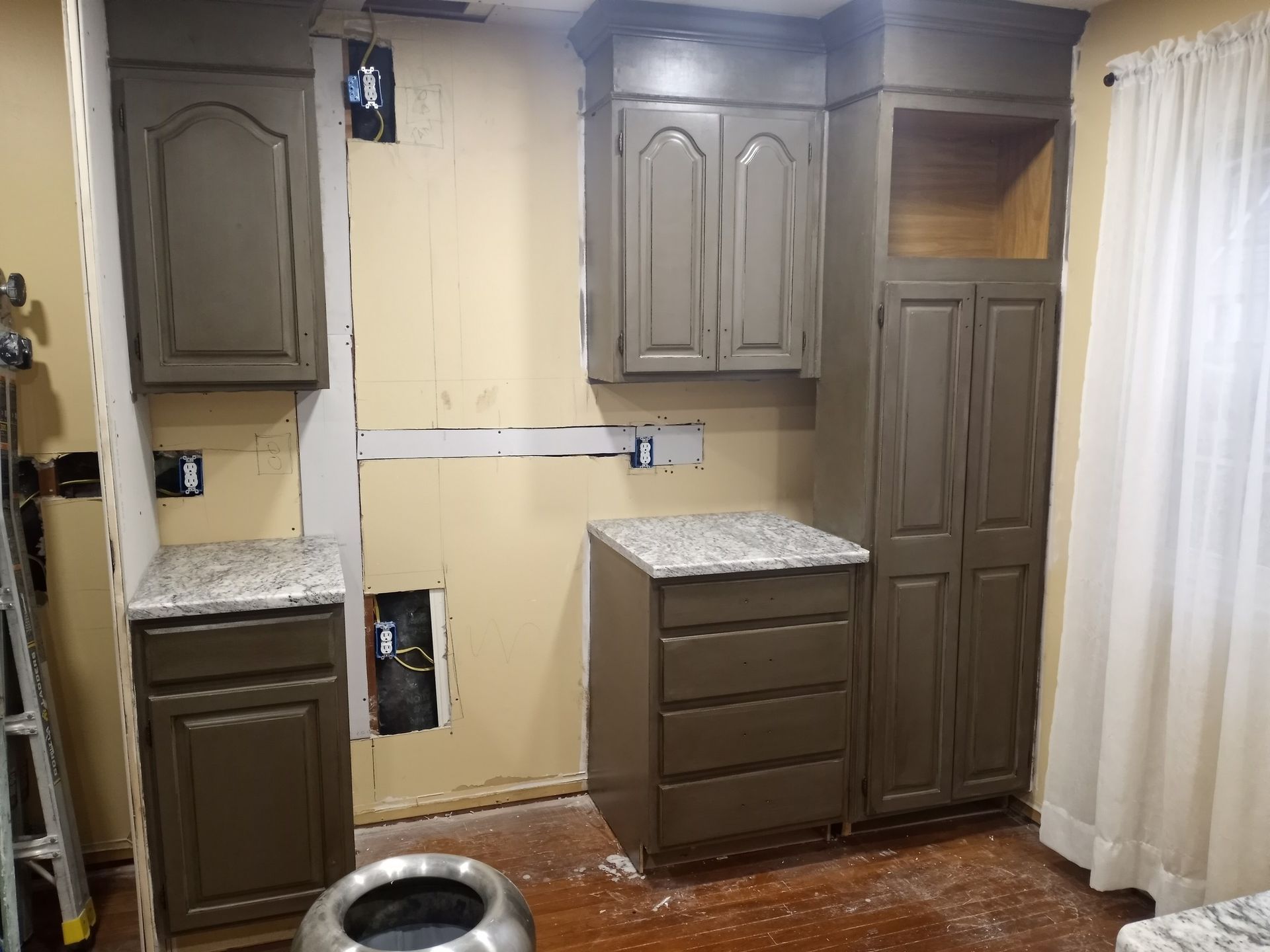 Partially renovated kitchen with gray cabinets, white walls, and exposed wall openings.