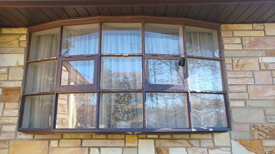 Curved bay window with dark trim on a stone exterior wall under a wood eave