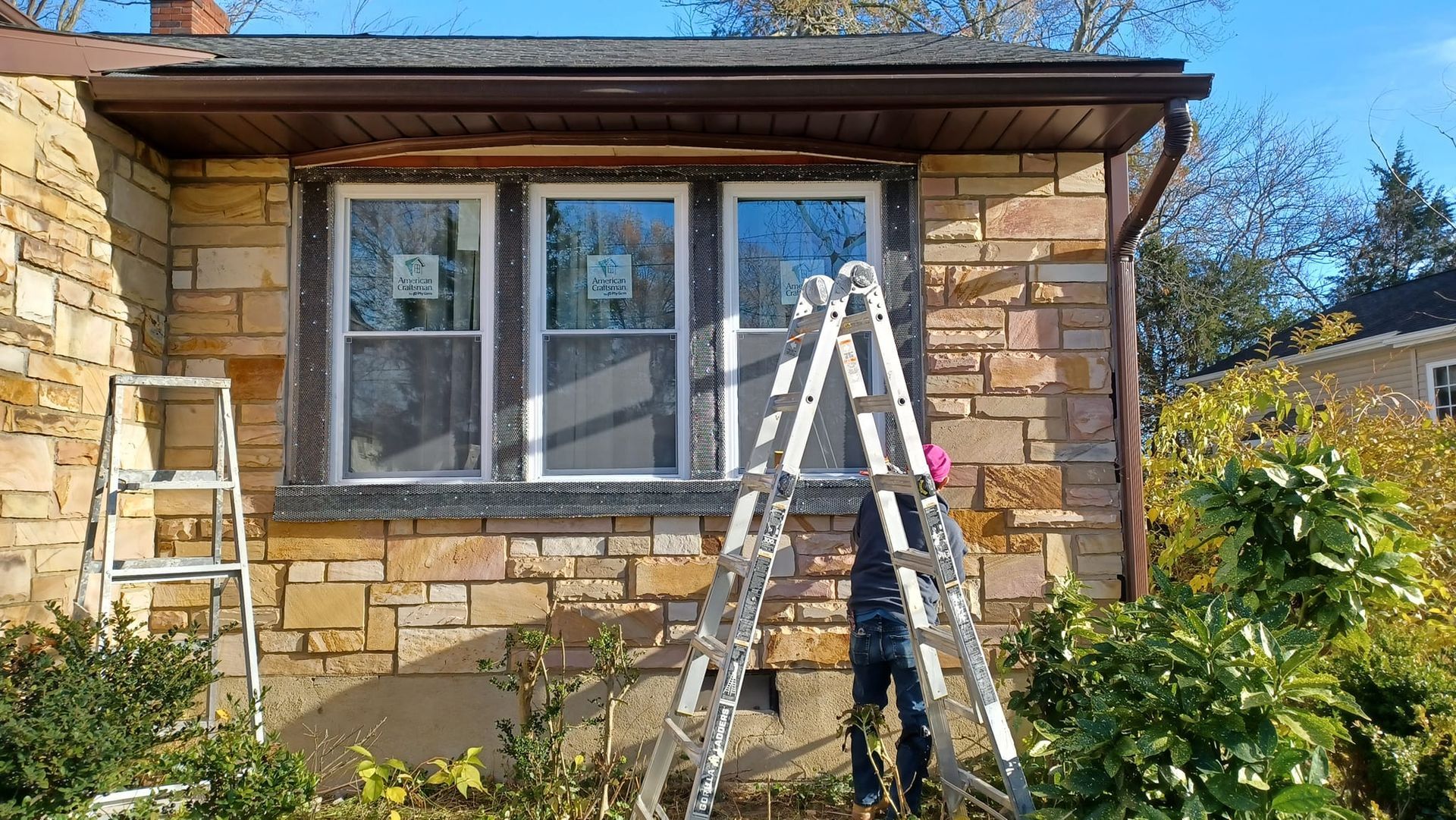 Ladders set up outside a stone house under a window, suggesting exterior maintenance work.