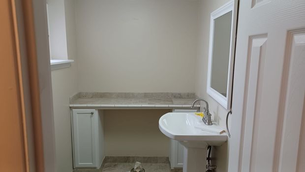 Small bathroom with a sink, countertop, and white doors in a narrow hallway.