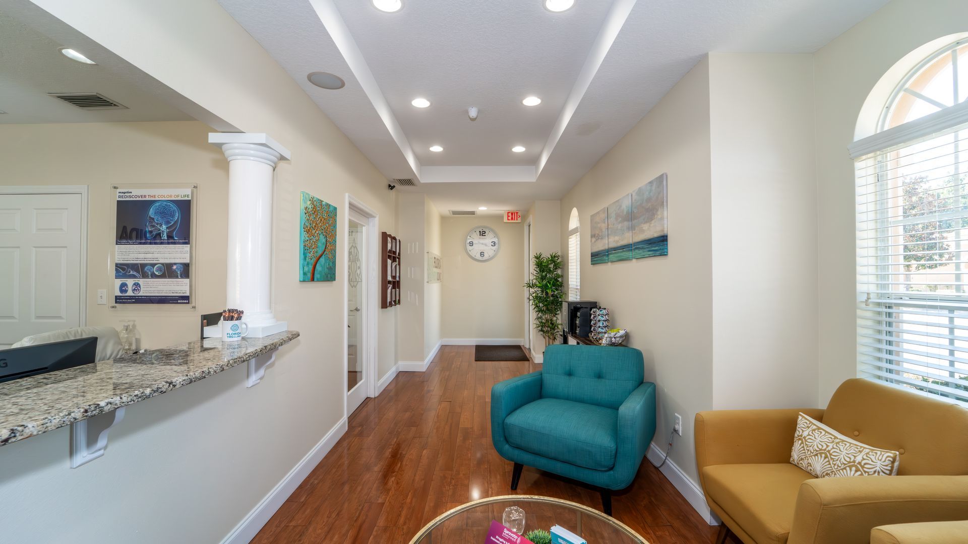 A bright office waiting area with a reception desk, seating, and a hallway leading to other rooms.