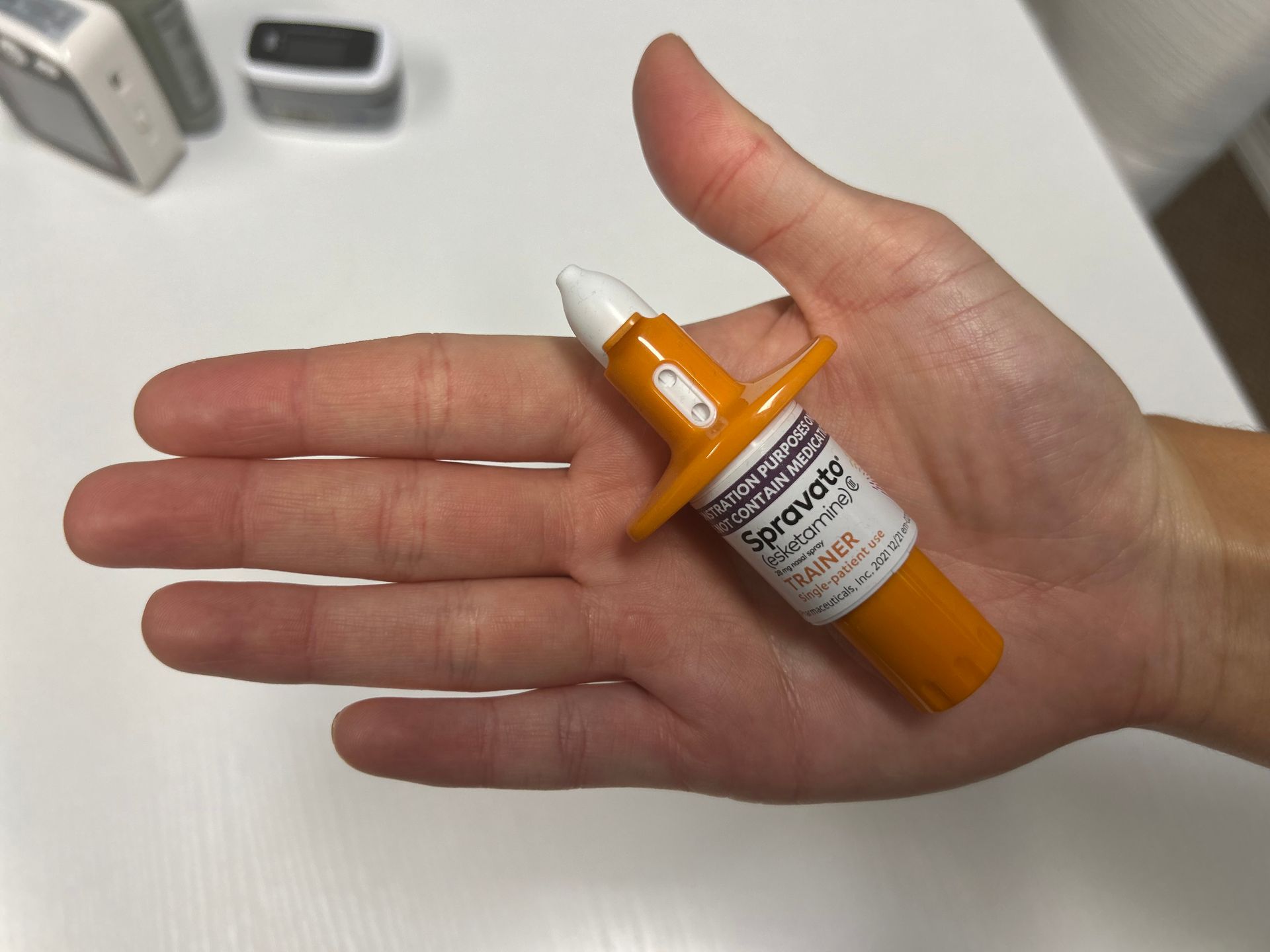 Person's hand holding an orange Narcan nasal spray.