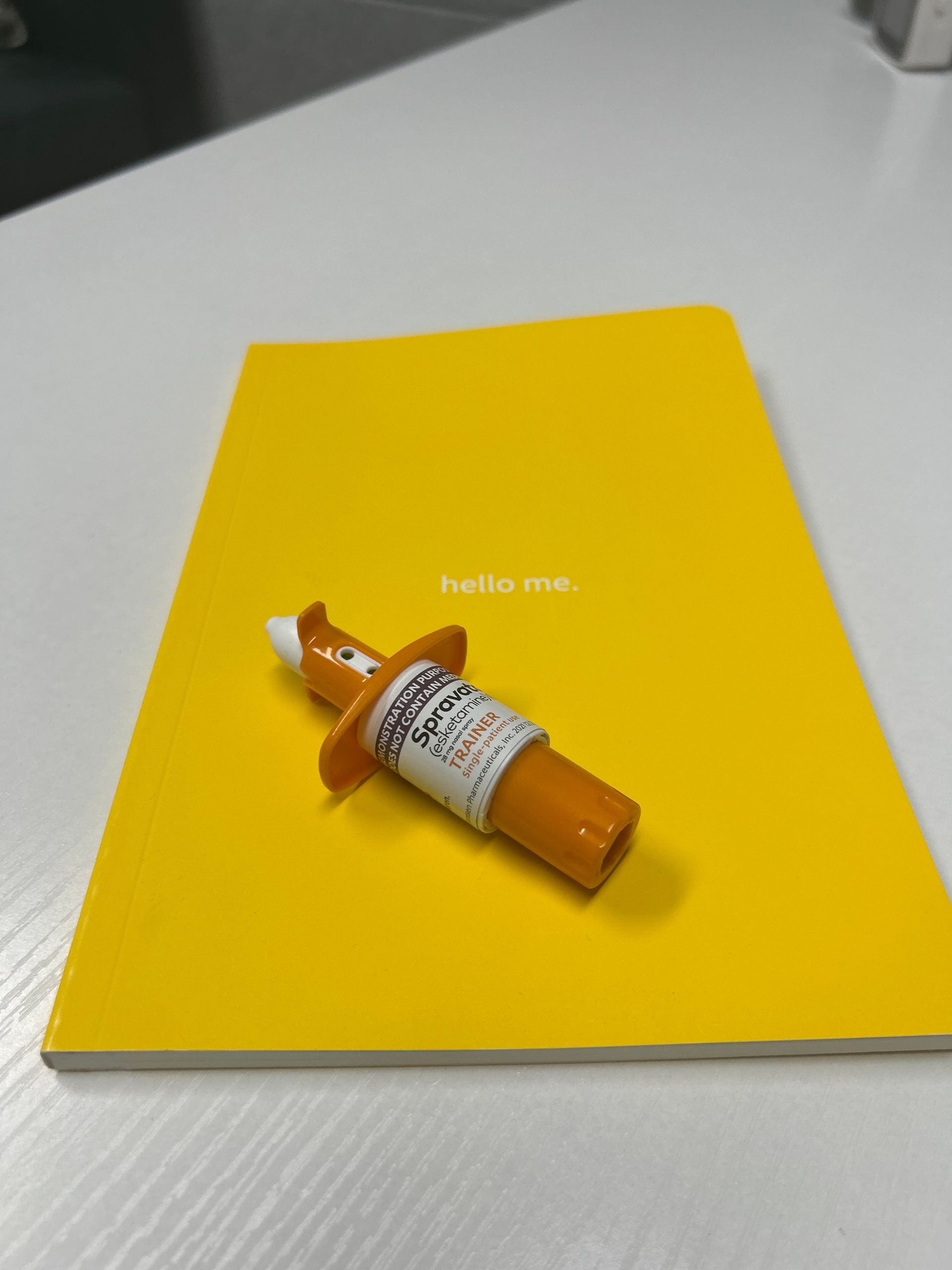 Orange epinephrine auto-injector sits on a closed yellow notebook on a white surface.