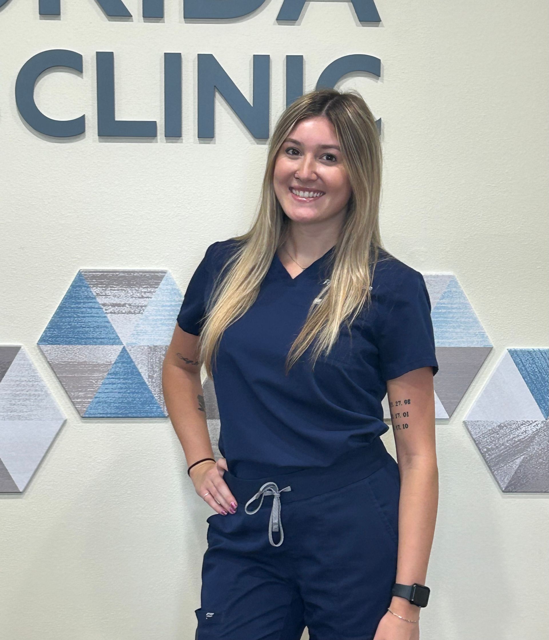 Woman in navy scrubs smiles, stands in front of