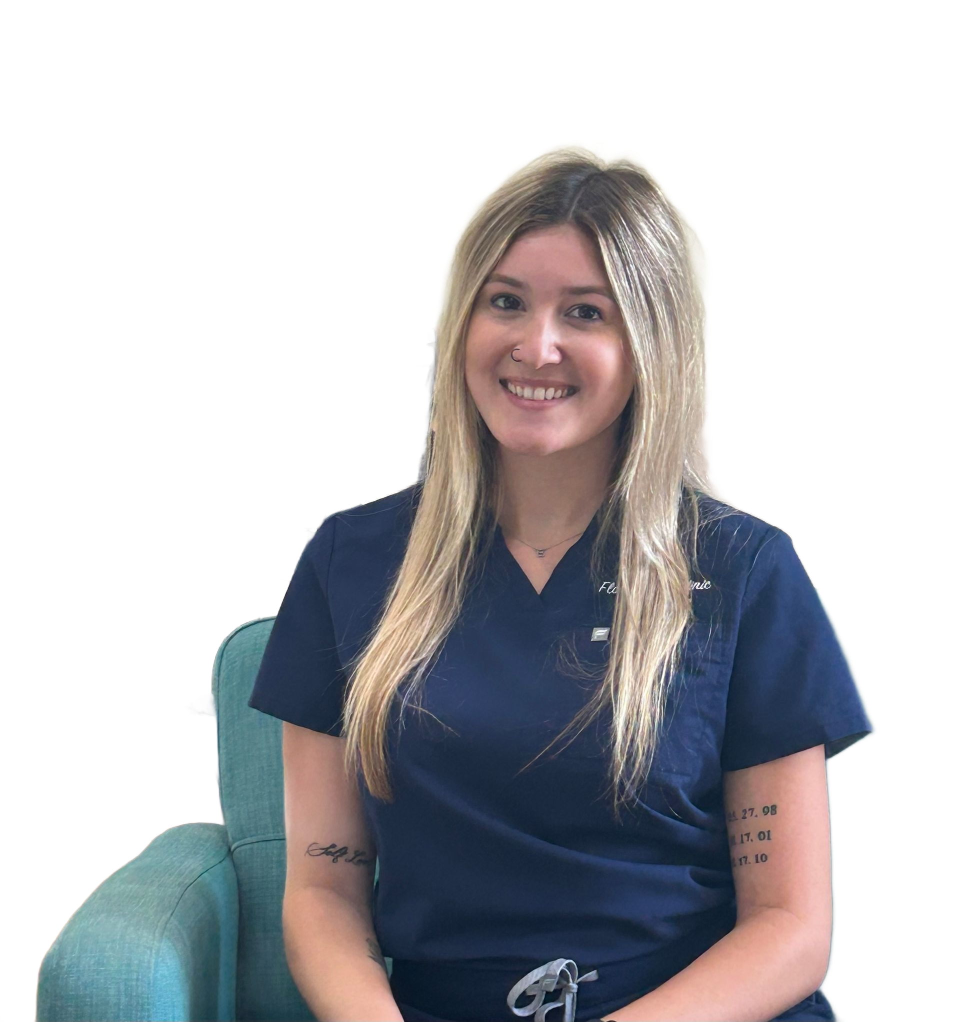 Woman with blonde hair, smiling, wearing blue scrubs, sitting in a teal chair.