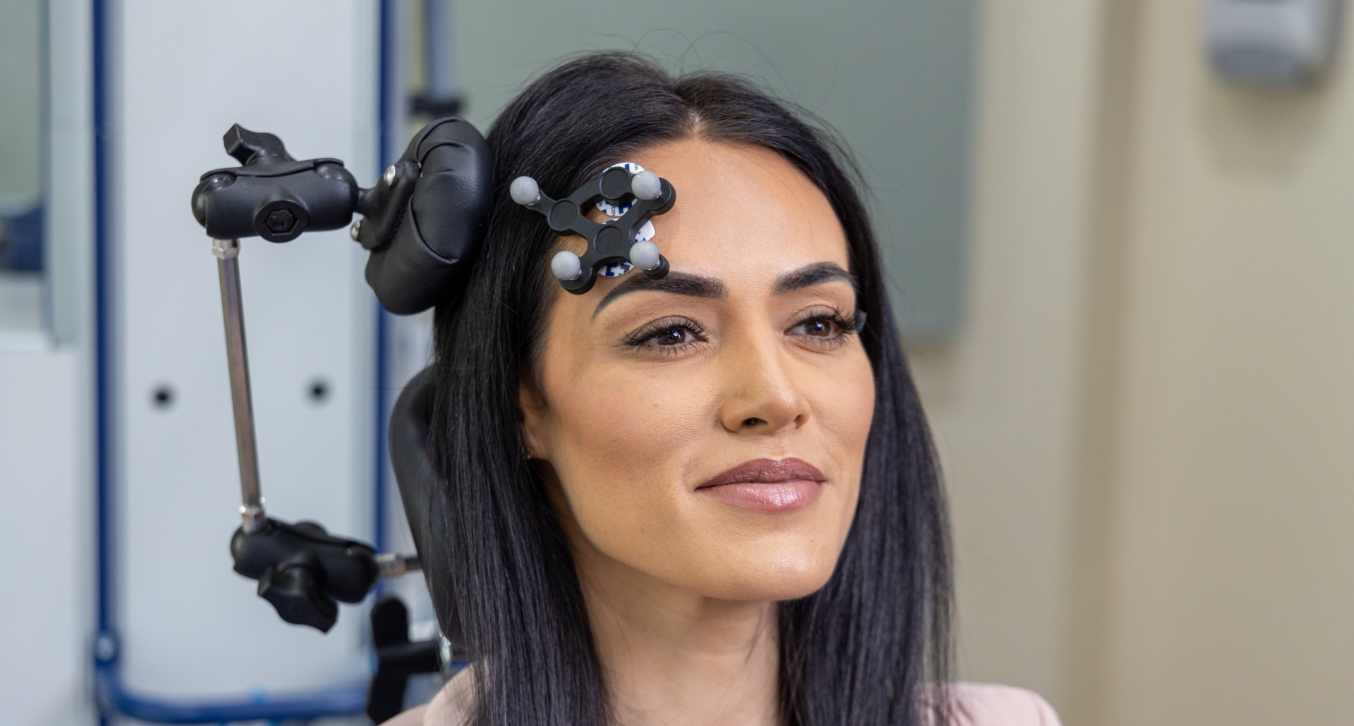 Woman with sensors attached to her head, possibly for medical research. She's smiling and indoors, possibly in a clinic.