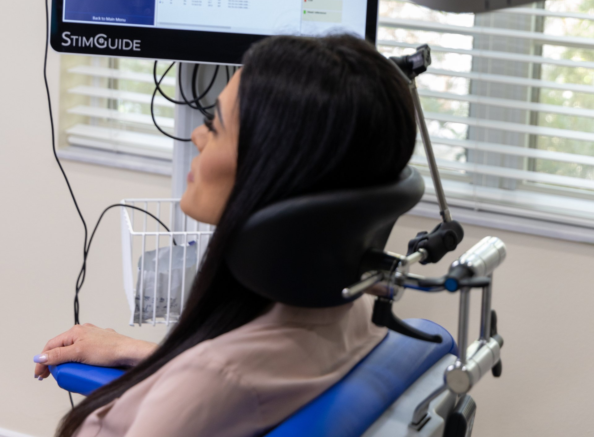Woman seated in a dental chair, head supported by a device, looking at a monitor. The setting appears to be a medical office.