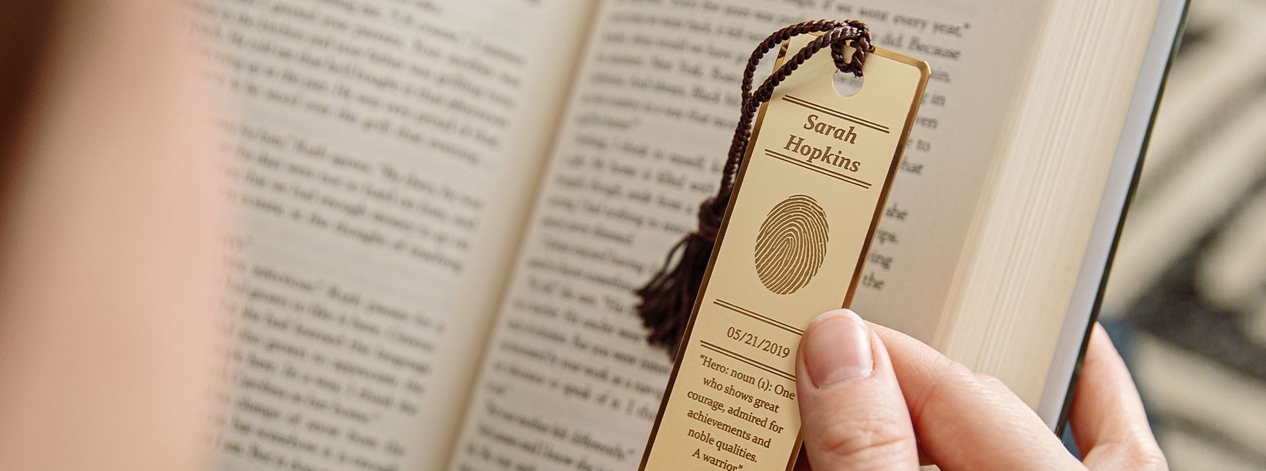 Person holding a book open with a wooden bookmark. The bookmark has text and a symbol.