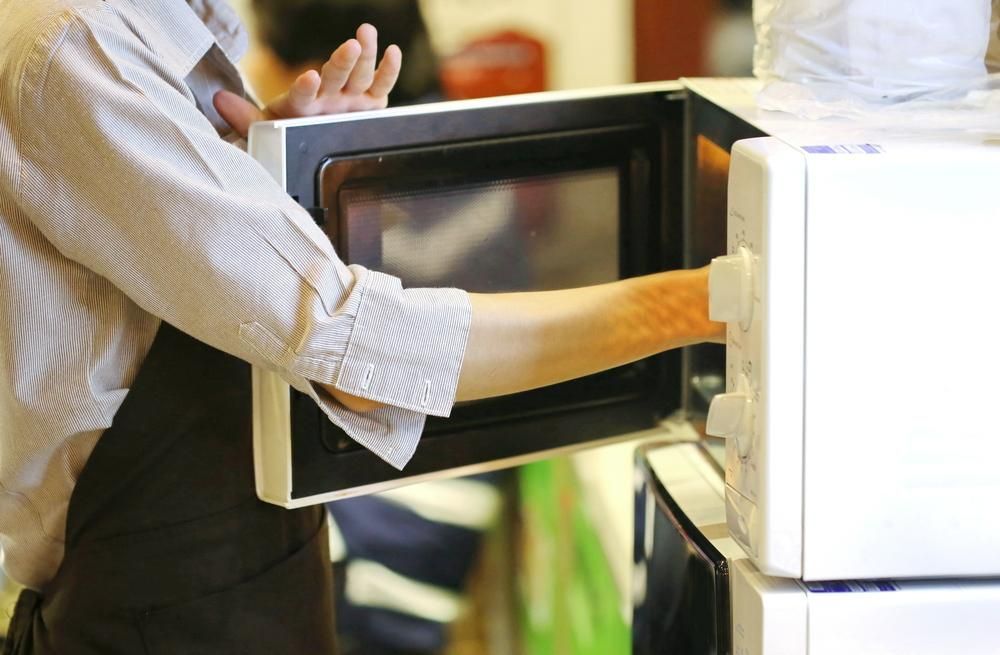 A Man Is Taking Something out Of a Microwave Oven — Mackay Cleaning & Packaging Supplies in Mackay, QLD