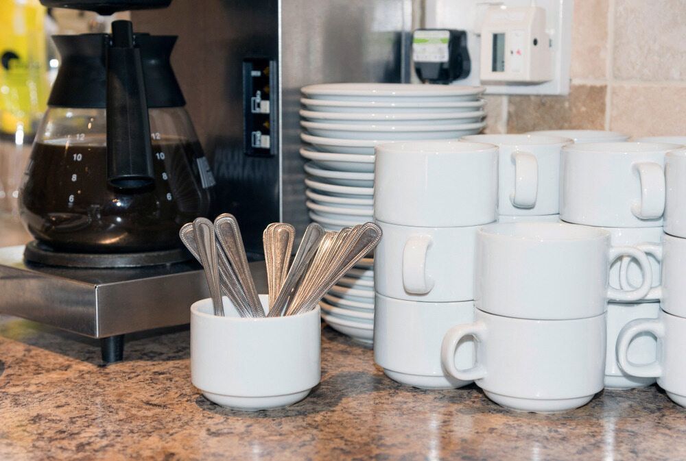 A Stack of Coffee Cups and Plates on a Counter Next to a Coffee Maker — Mackay Cleaning & Packaging Supplies in Mackay, QLD