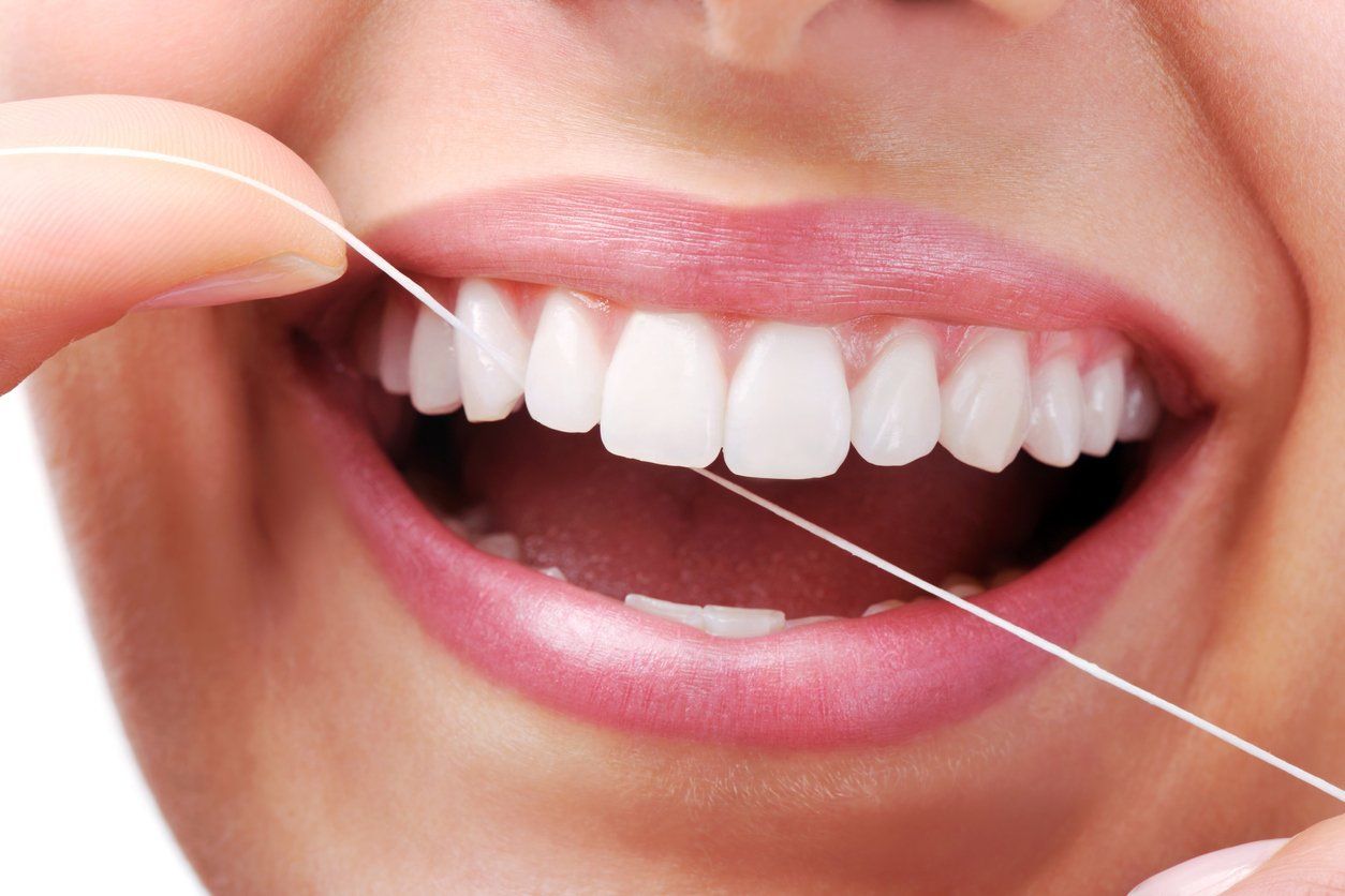 woman flossing her teeth while smiling