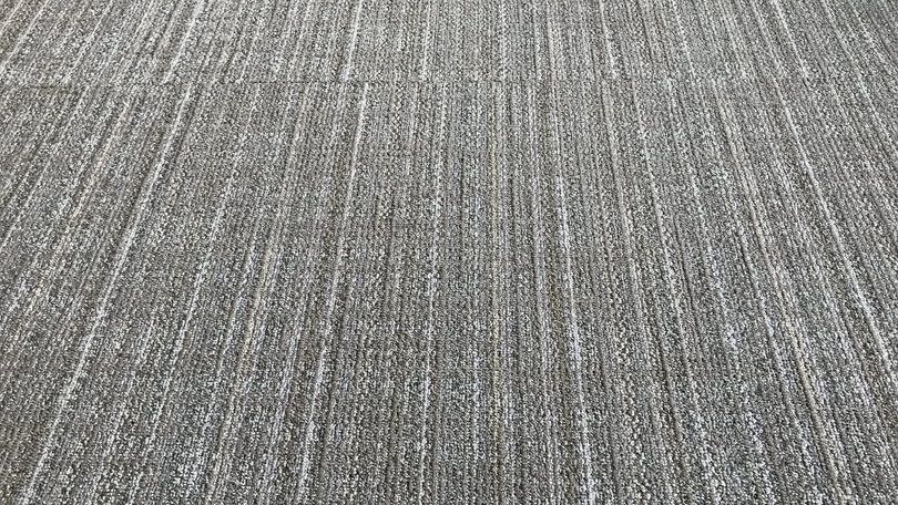 A close-up view of textured gray carpet tiles with a linear, vertical pattern.