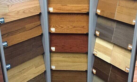 A retail display rack showcasing various wood flooring samples in a wide range of grain patterns and brown tones.