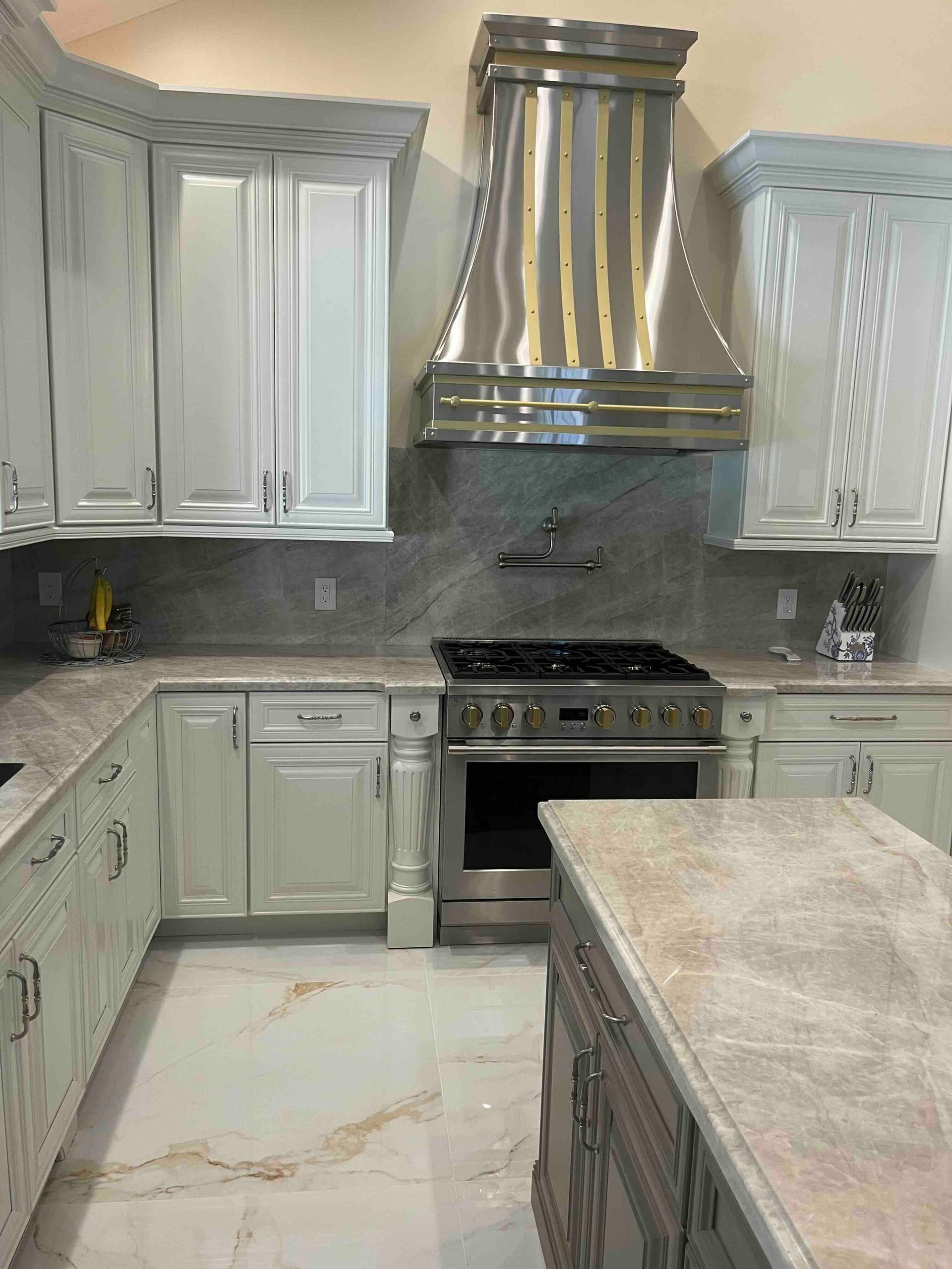 A kitchen with white cabinets , a stove , a sink , and a hood.
