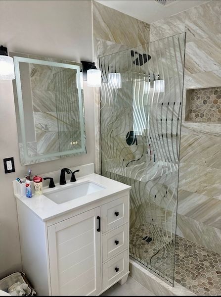 A bathroom with a sink , mirror and walk in shower.