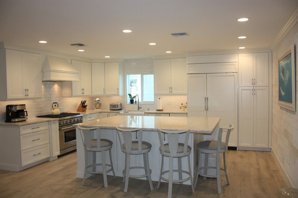 A kitchen with white cabinets , granite counter tops , stools and a large island.
