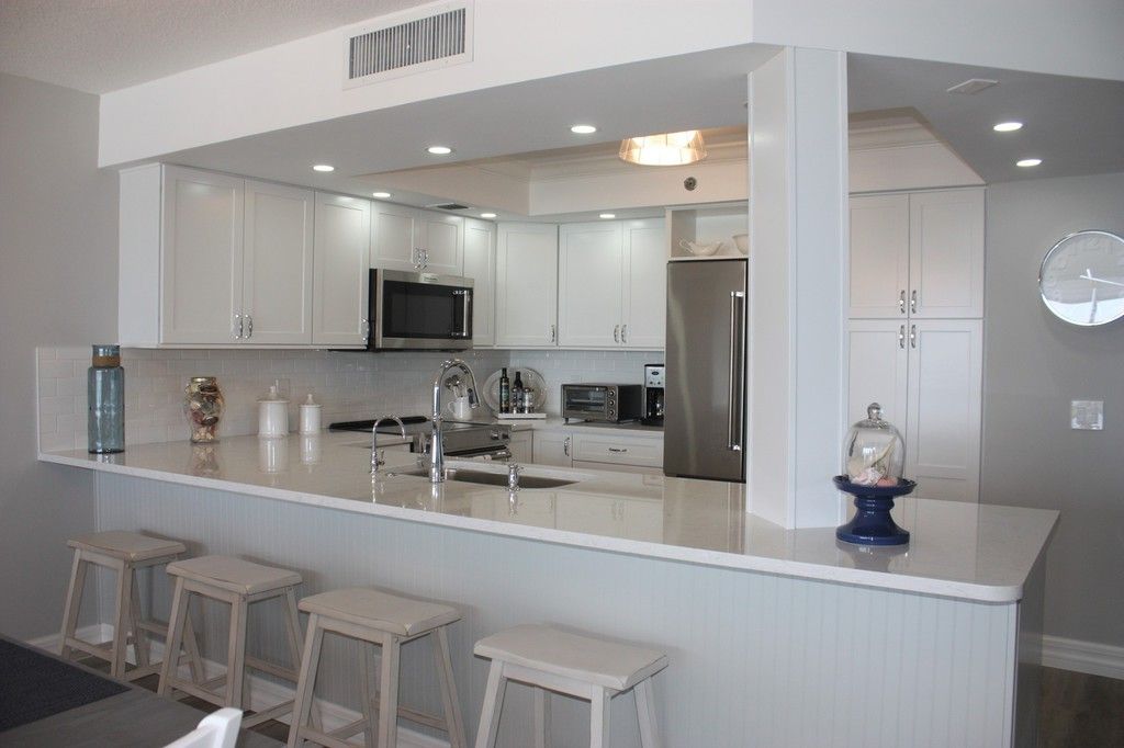 A kitchen with white cabinets and stools and a long counter.