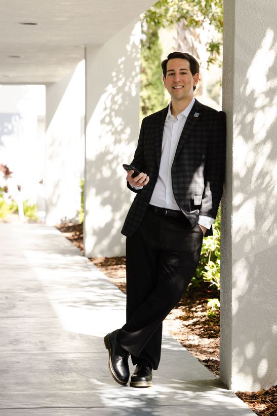 A man is sitting leaning against a pillar, cellphone in hand. 
