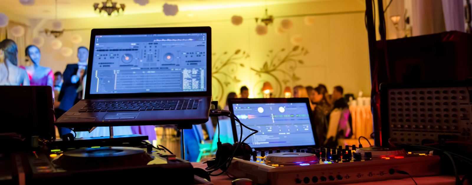 Party DJ booth with two laptops showing the virtual music turntables and party guests in the background.