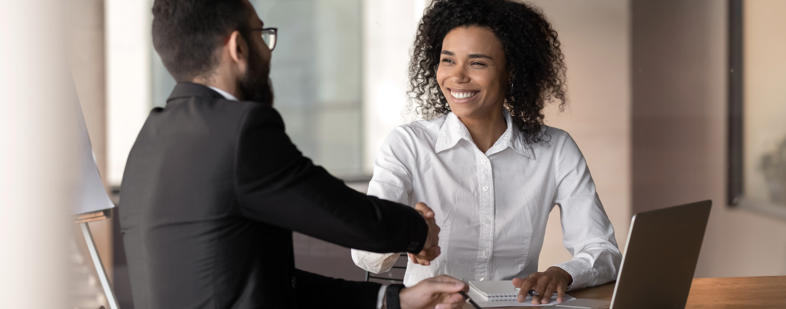 Two professionals smiling and shaking hands.