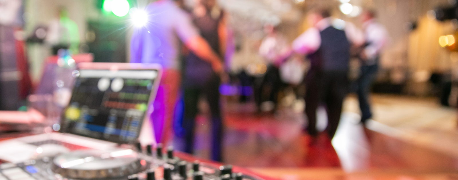 Wedding DJ booth at wedding reception with guests dancing to music.