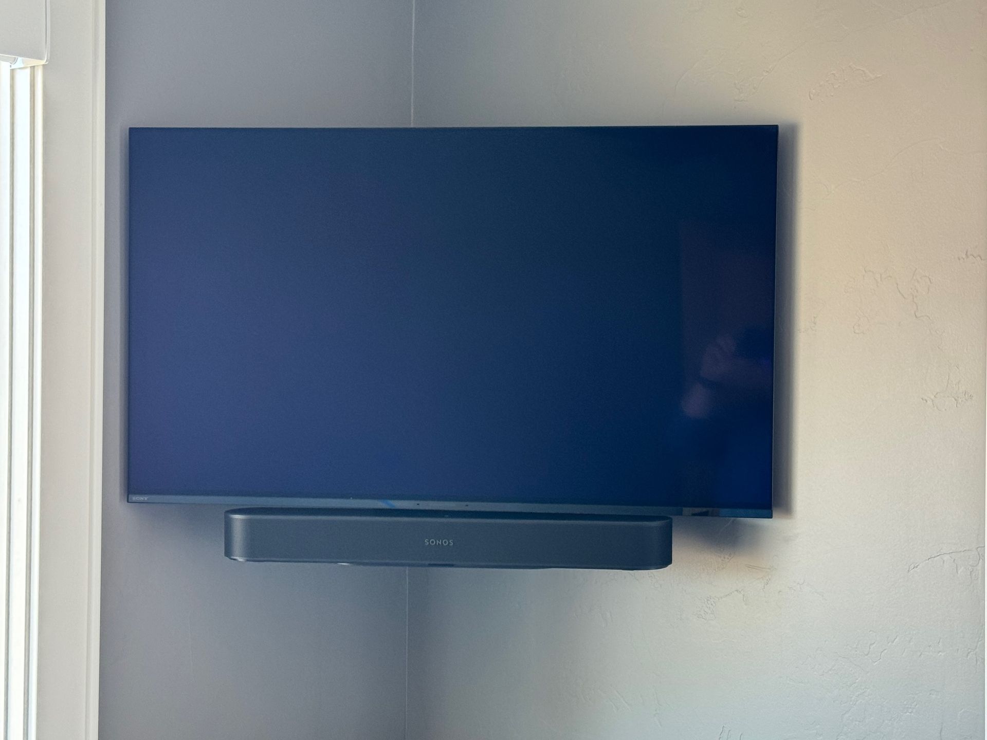 A flat-screen TV and soundbar mounted on a gray wall near a window corner.