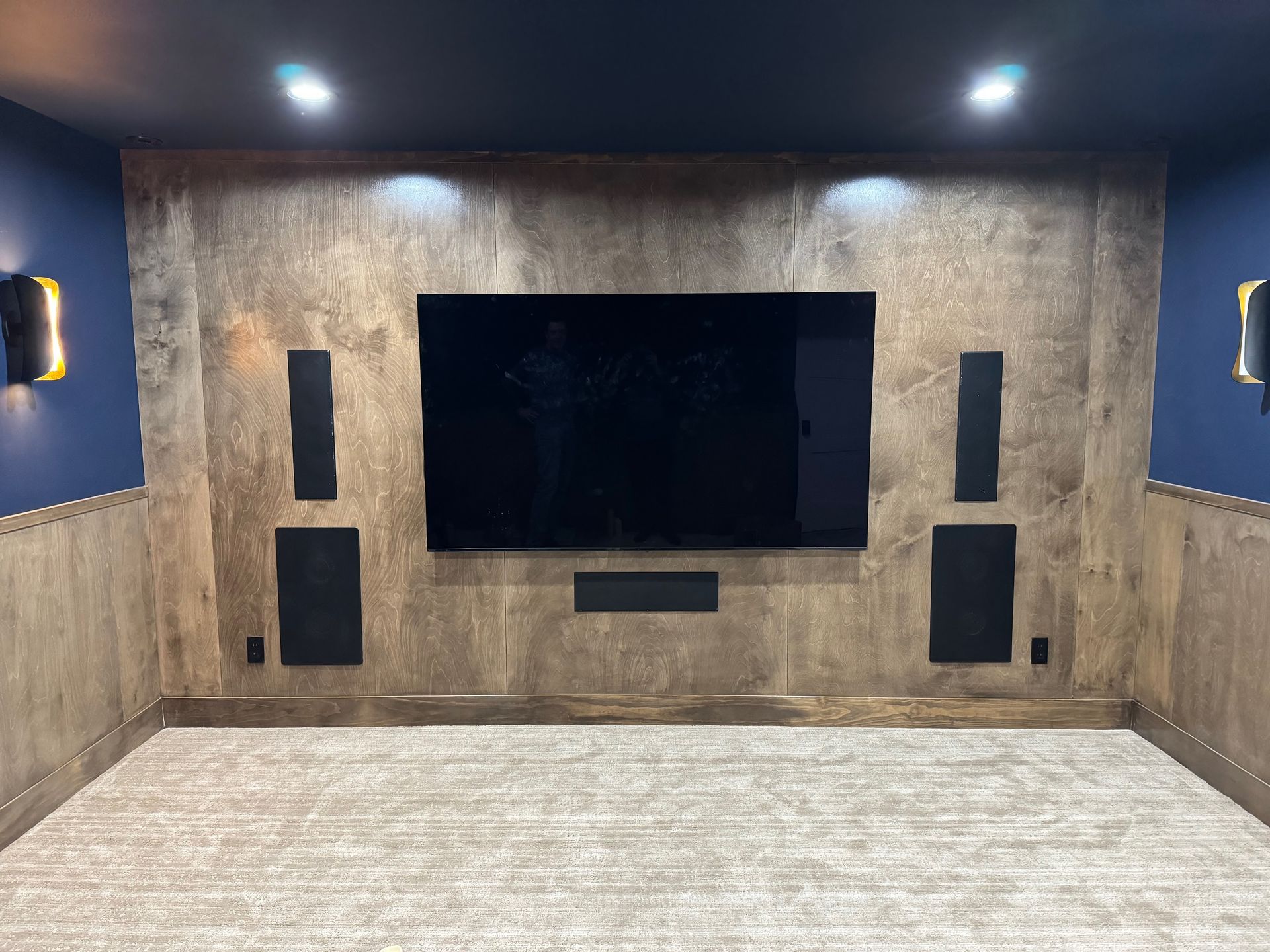 Home theater setup: large TV, speakers, and wall-mounted lights on a textured wall; blue side walls; gray carpet.