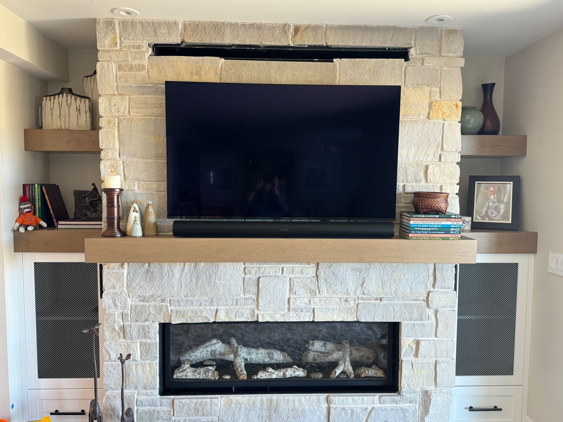 Stone fireplace with a TV, soundbar, and floating shelves, built into a wall.