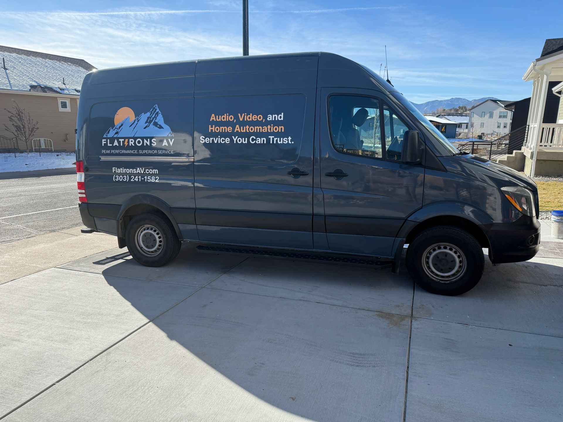 Dark gray van parked on a driveway with text advertising 