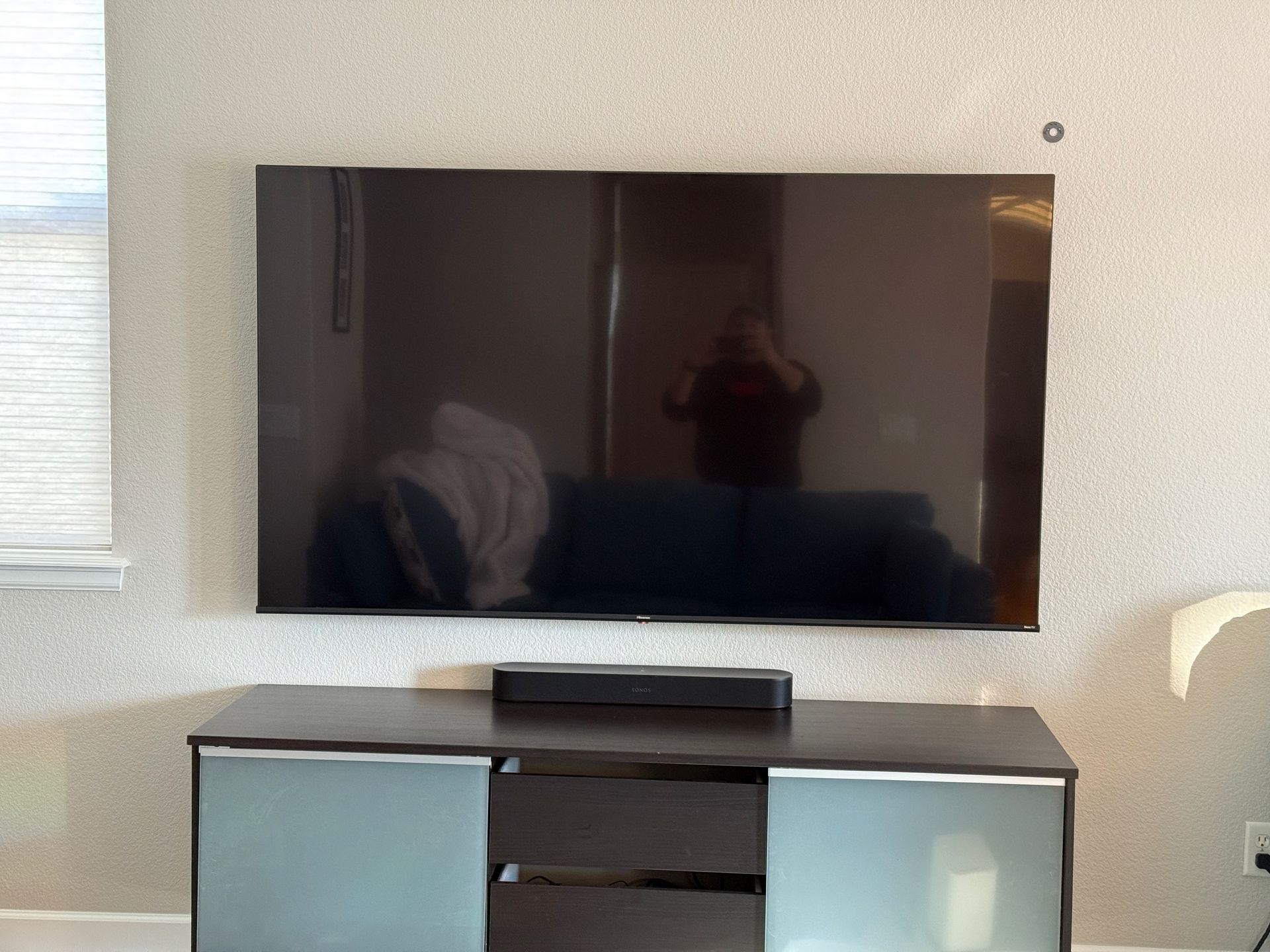 A large TV is mounted above a dark cabinet, with a soundbar centered below the screen.