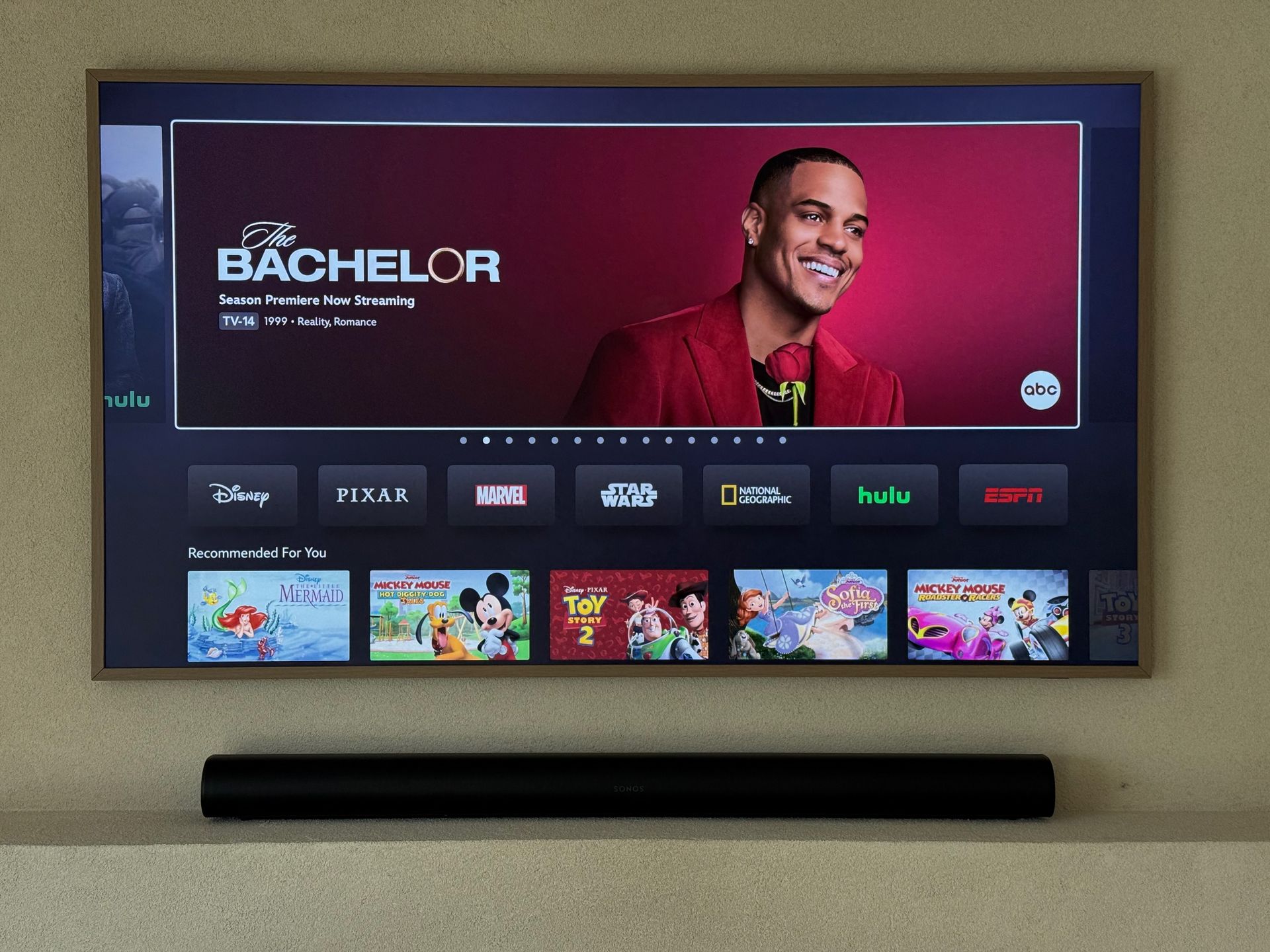 Television screen displaying The Bachelor show, surrounded by streaming app icons. Soundbar below.