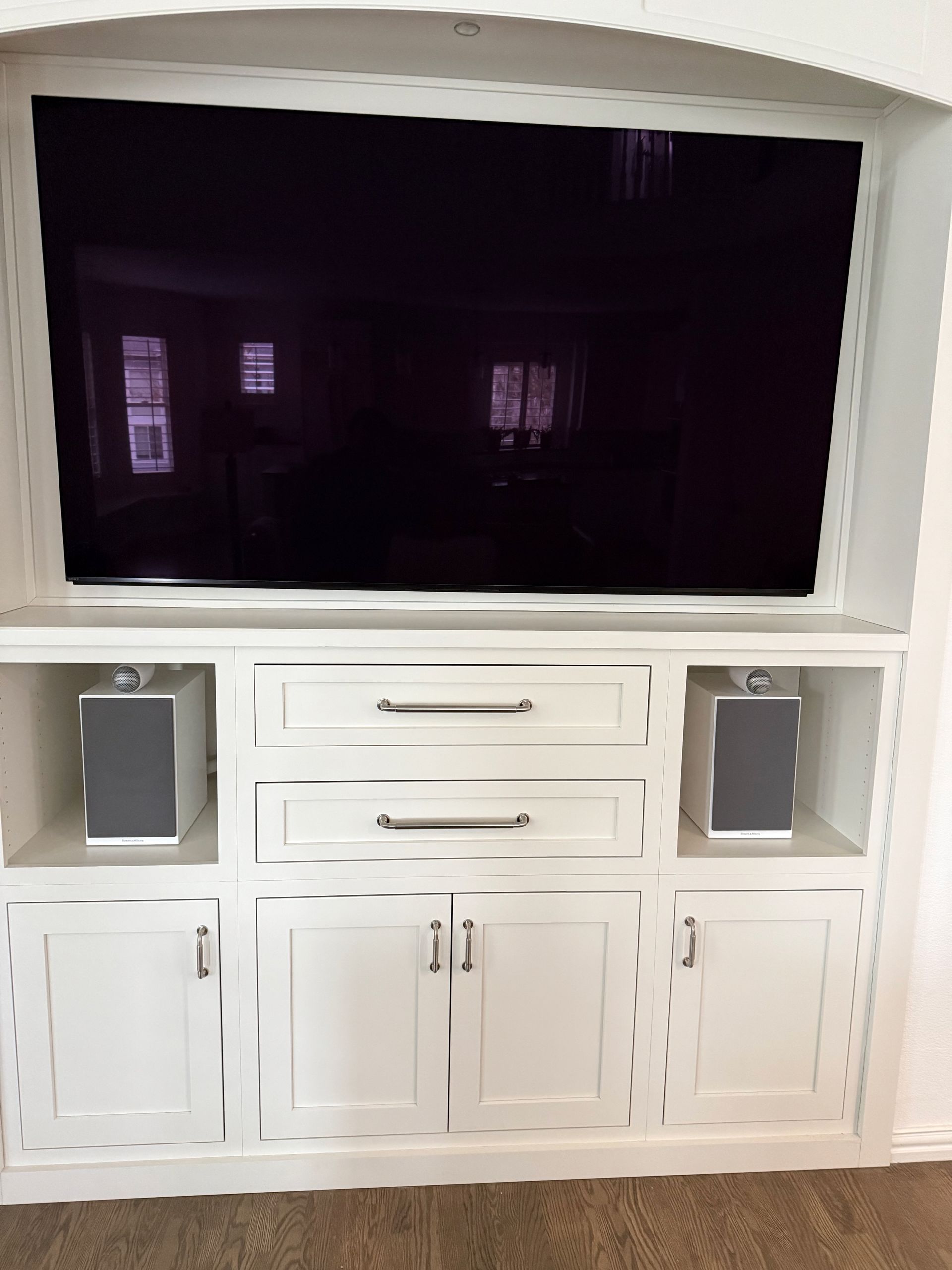 White built-in entertainment center with TV, drawers, cabinets, and speakers.
