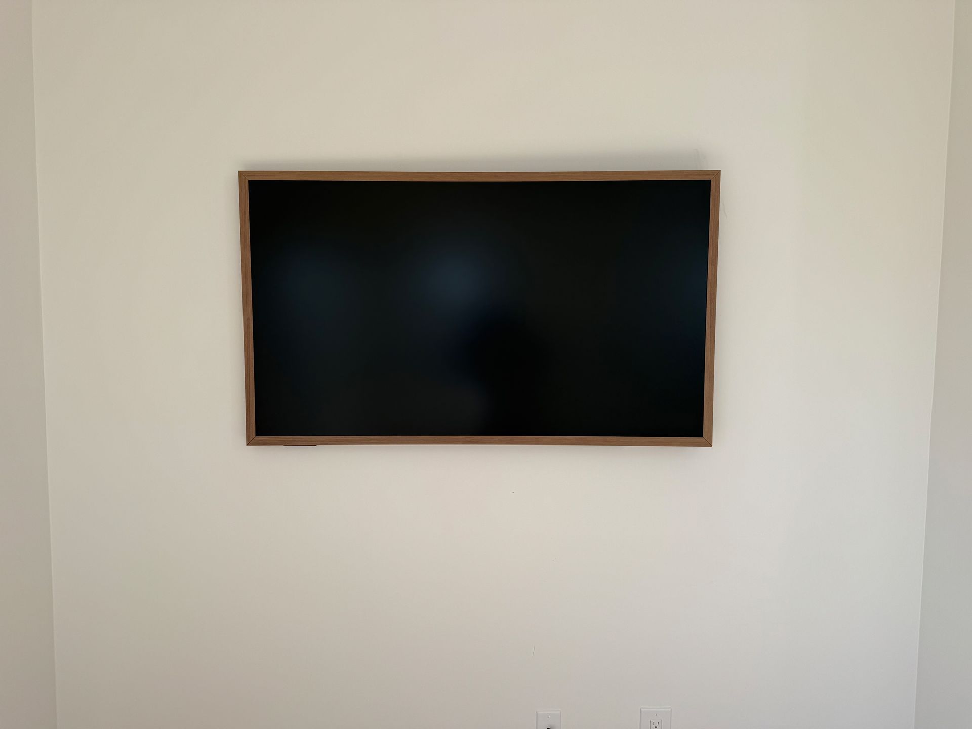 A flat-screen TV with a brown frame mounted on a white wall.