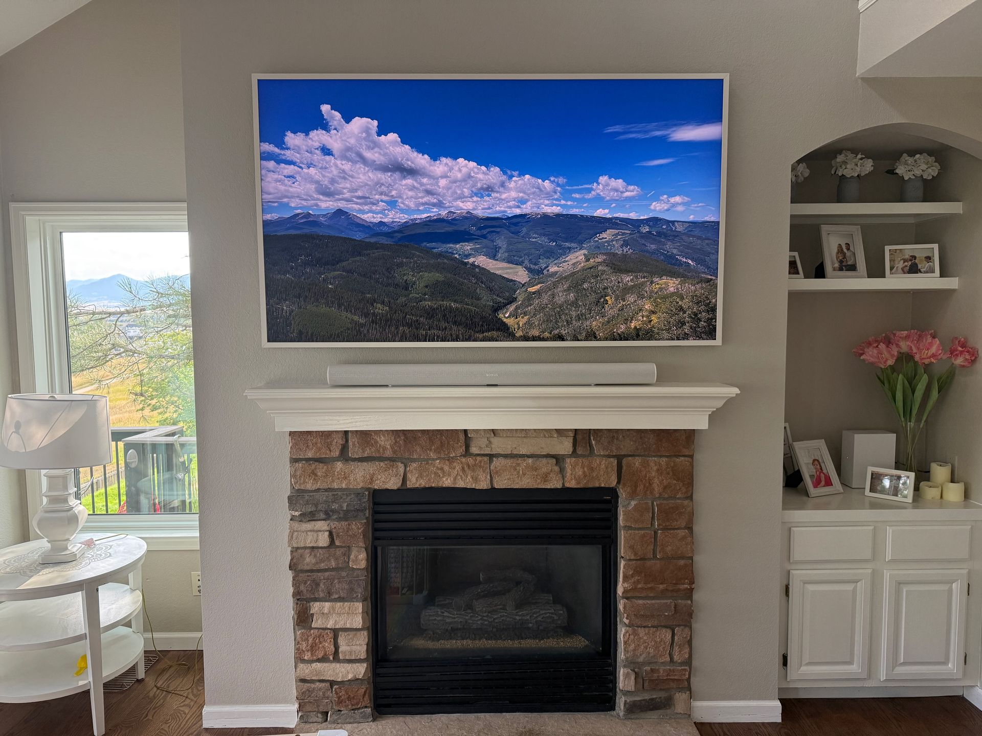 A fireplace with a mounted TV above, soundbar, built-in shelving, and a window.