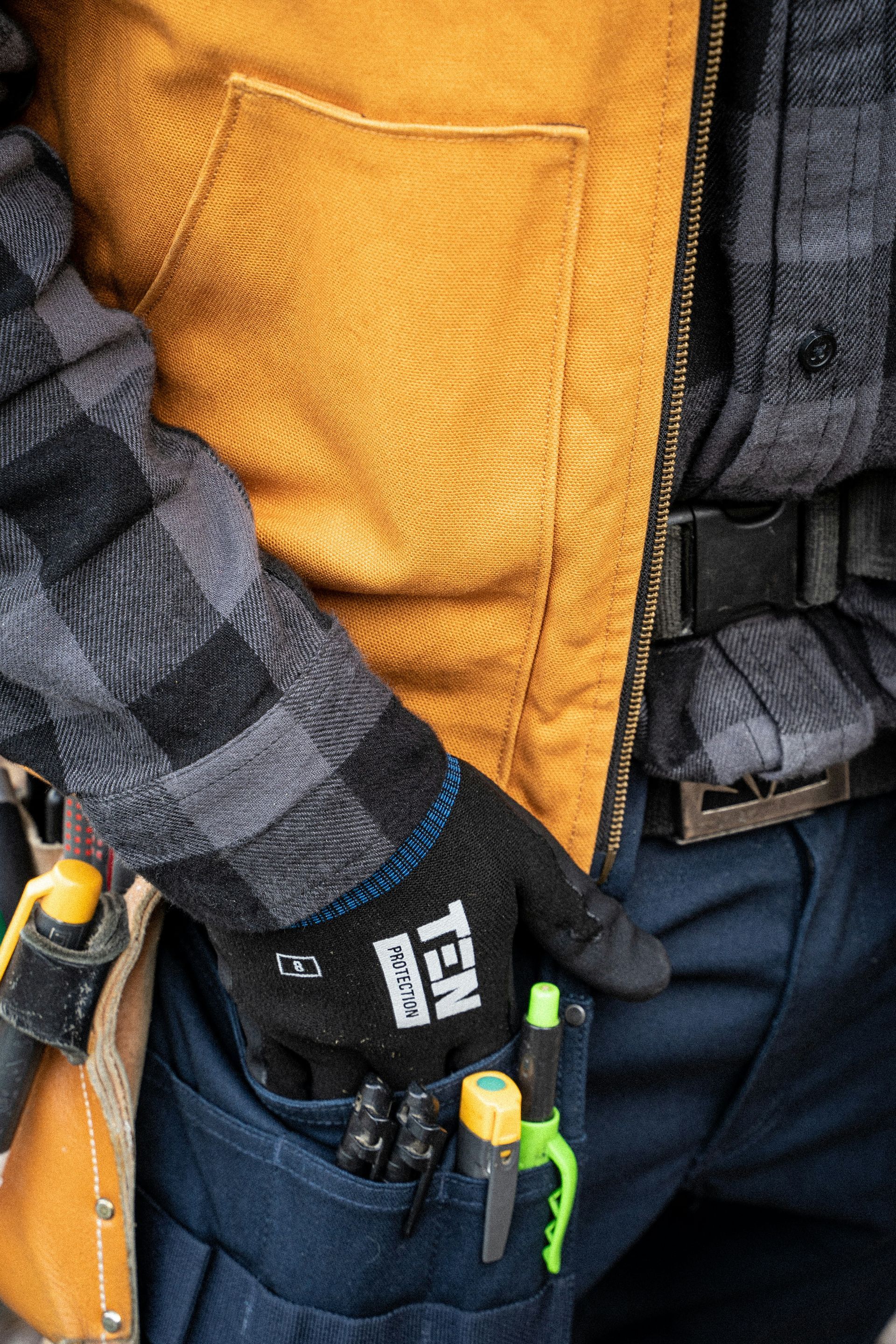 Person in plaid shirt and work vest with gloves, tools in pocket.