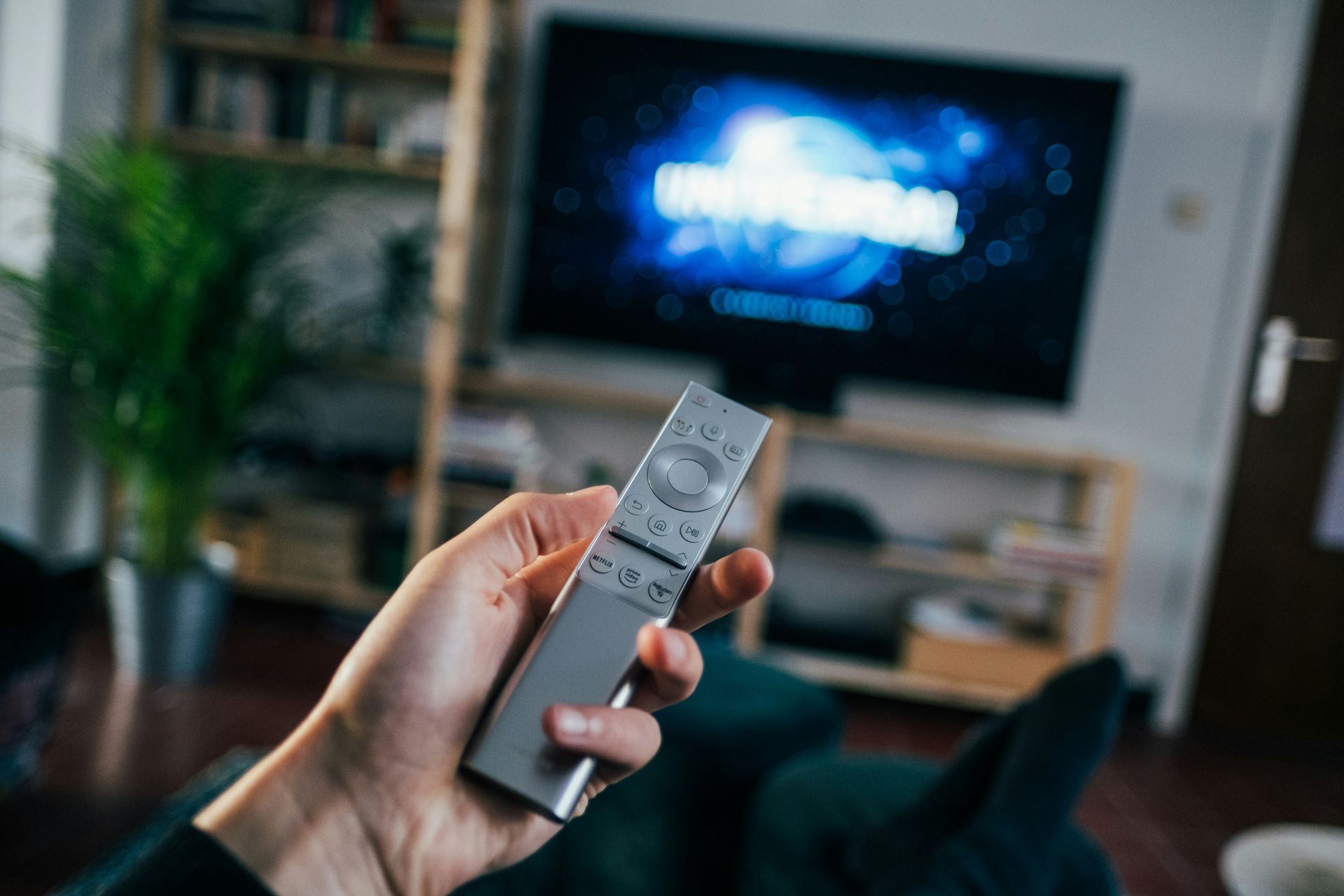 Hand holding a remote, pointing towards a television displaying the Universal logo.