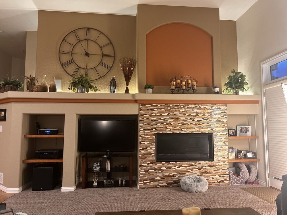 Living room with stone fireplace, TV, clock, and decorative shelving.
