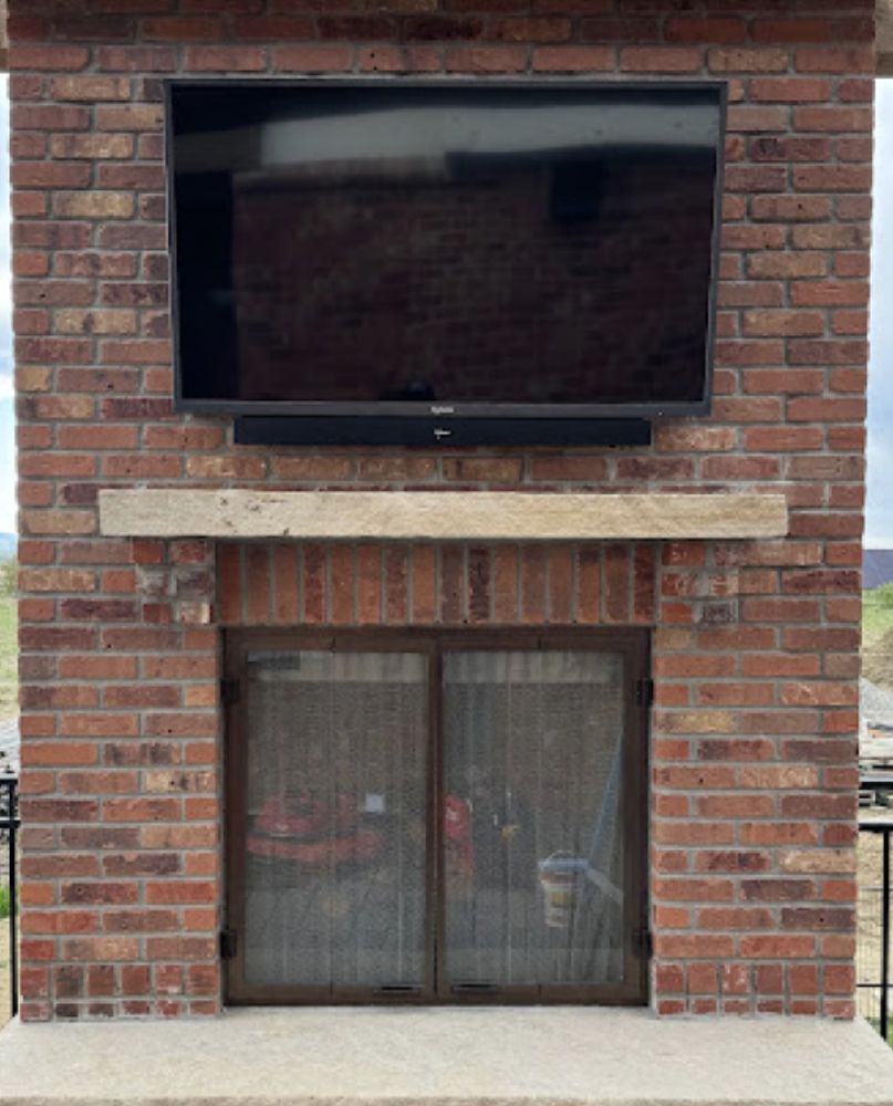 Brick fireplace with mounted TV and soundbar; wooden mantle and mesh doors.