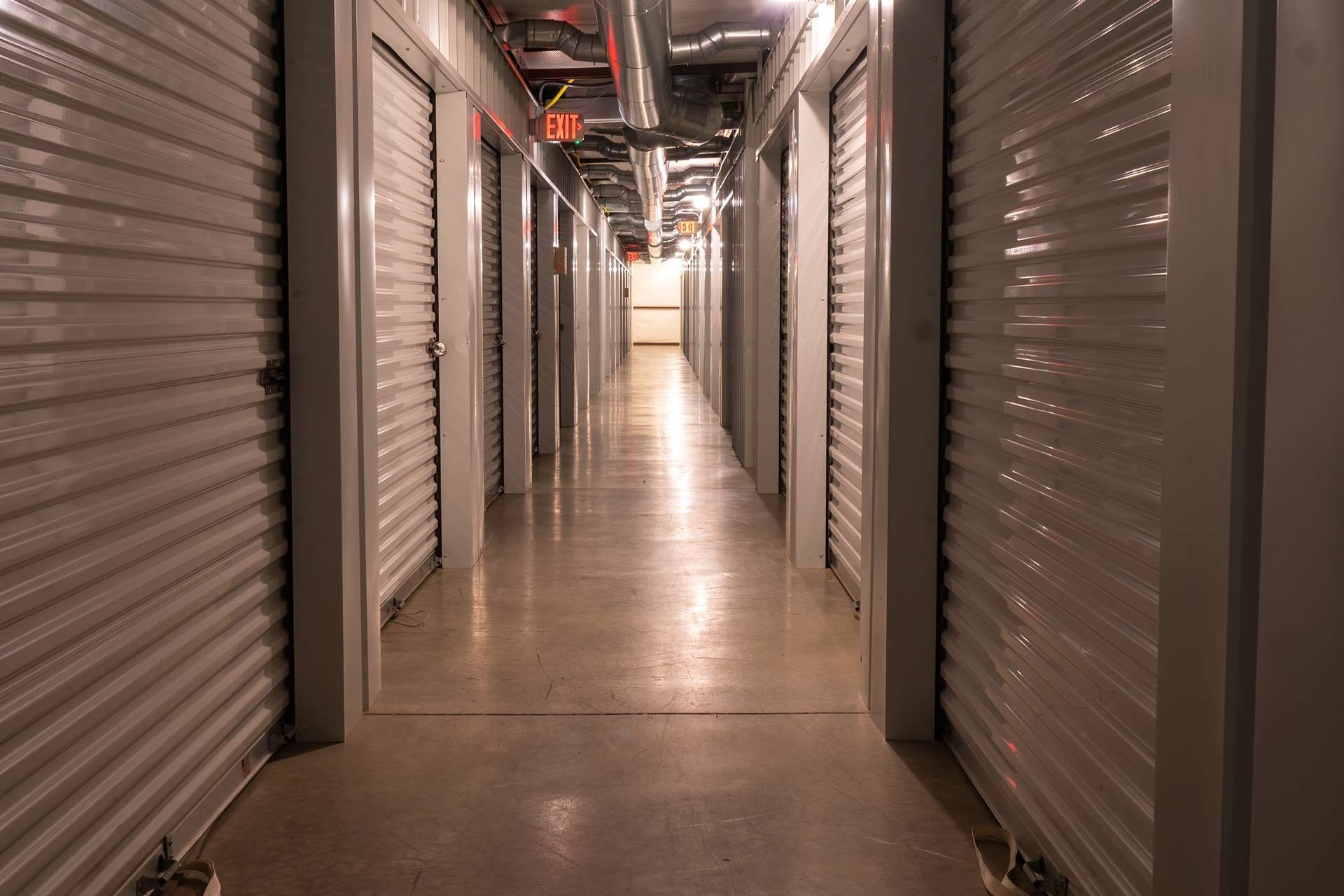 Interior climate controlled rental storage units with exit signs and locked metal roller doors.