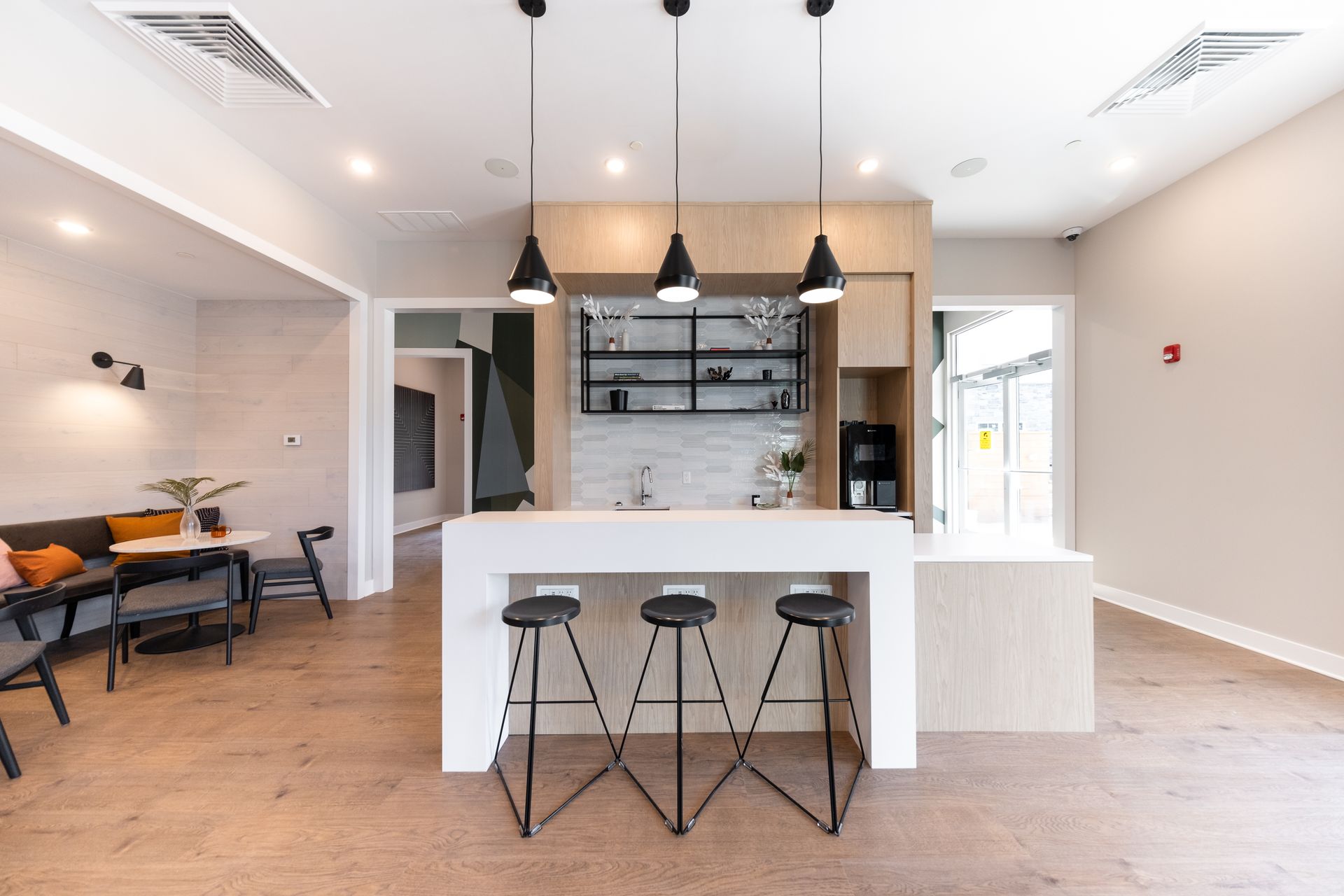 Modern kitchen with a white countertop and bar stools. Black pendant lights hang above.