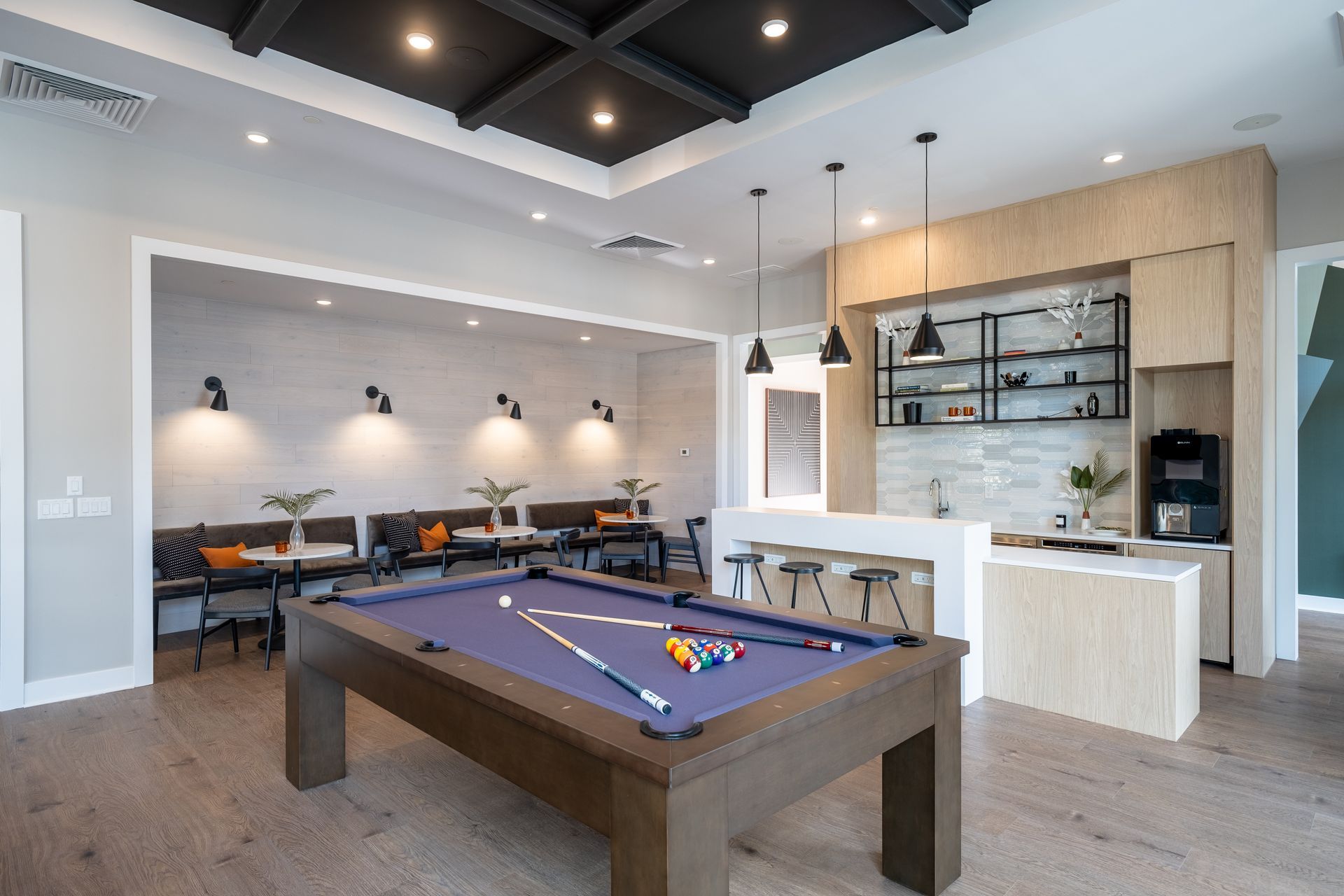 Game room with pool table, bar, seating area, and wooden flooring.