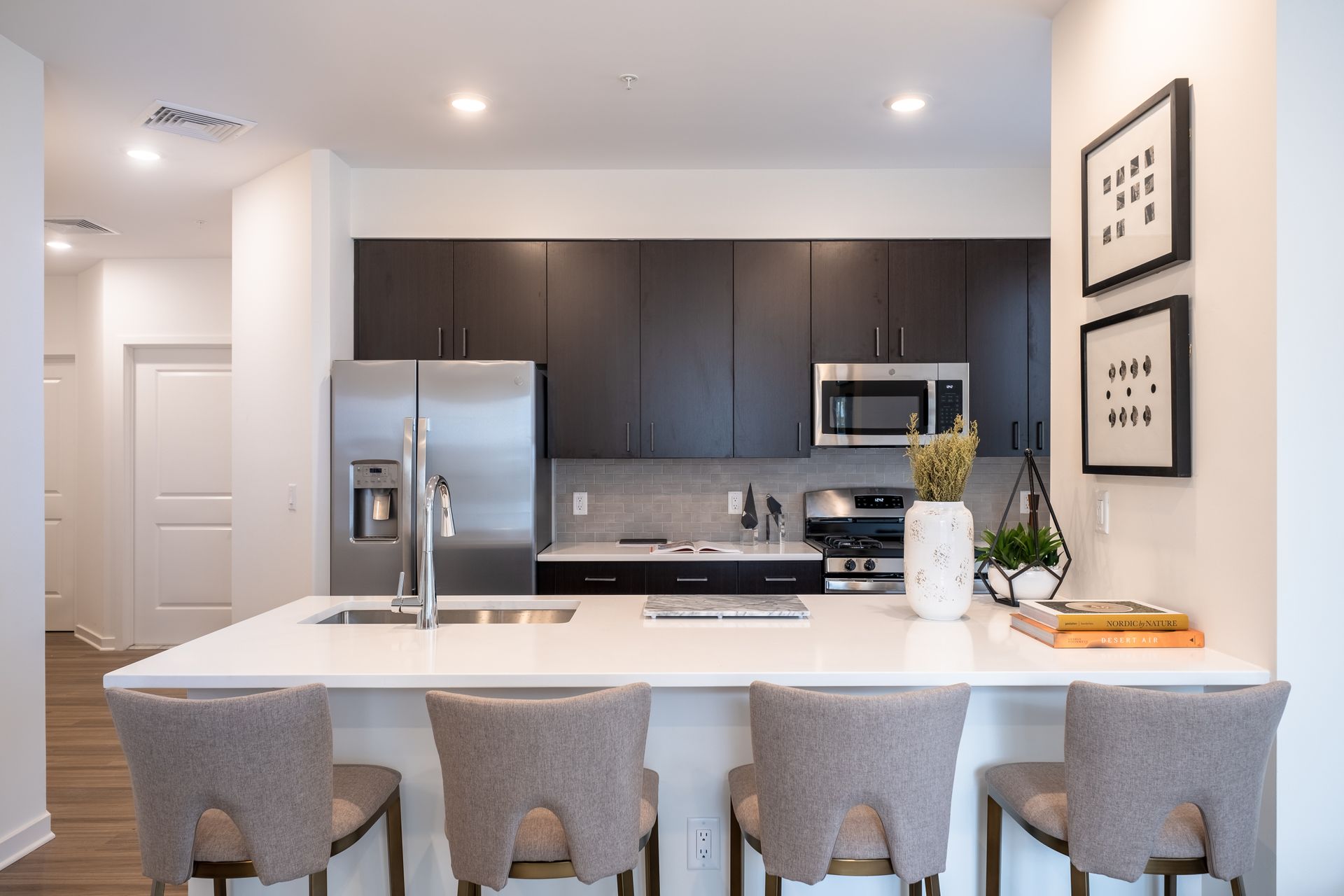 Modern kitchen with white island, dark cabinets, stainless steel appliances, and upholstered bar stools.